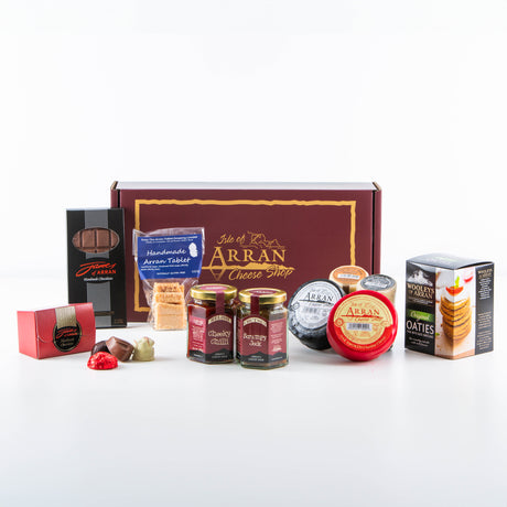 A gift box from the Isle of Arran Cheese Shop containing various cheeses, chutneys, oatcakes, chocolates, and fudge, all elegantly arranged. The box has a maroon color with gold text and illustrations.