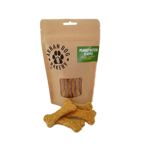 A brown paper bag labeled "Arran Dog Bakery" presents Apple & Peanut Butter Arran Dog Biscuits in a display window, crafted with vegetarian ingredients. Three handmade treats from Brodick are set against a white background.