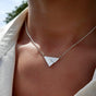 Close-up of a person wearing the sterling silver Little Cir Mhor Pendant Necklace from Isle of Arran, featuring a mountain design, resting on their chest and partially covered by a white, unbuttoned shirt collar.