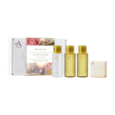 The After the Rain Discovery Gift Set by Arran offers elegant gift packaging that includes three small bottles labeled body wash, shampoo, and body lotion, along with a soap bar. The packaging is adorned with an exquisite design featuring rose and natural elements and is branded with the "After the Rain" label.