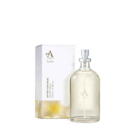 A 100ml glass spray bottle of "After The Rain Room Spray" containing light yellow liquid is placed beside its white packaging box. The box features a minimalistic design with the "Arran Home" logo and product information.