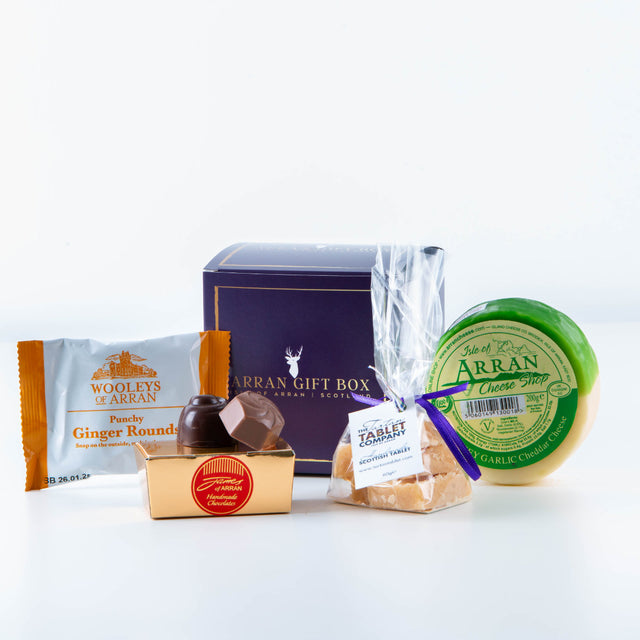 The Wee Big Taste Arran Gift Box, drawing inspiration from the Isle of Arran, includes a delightful assortment: ginger rounds, a box of chocolates, a wedge of cheese with green wax, and shortbread labeled "Cornish Seasalt.