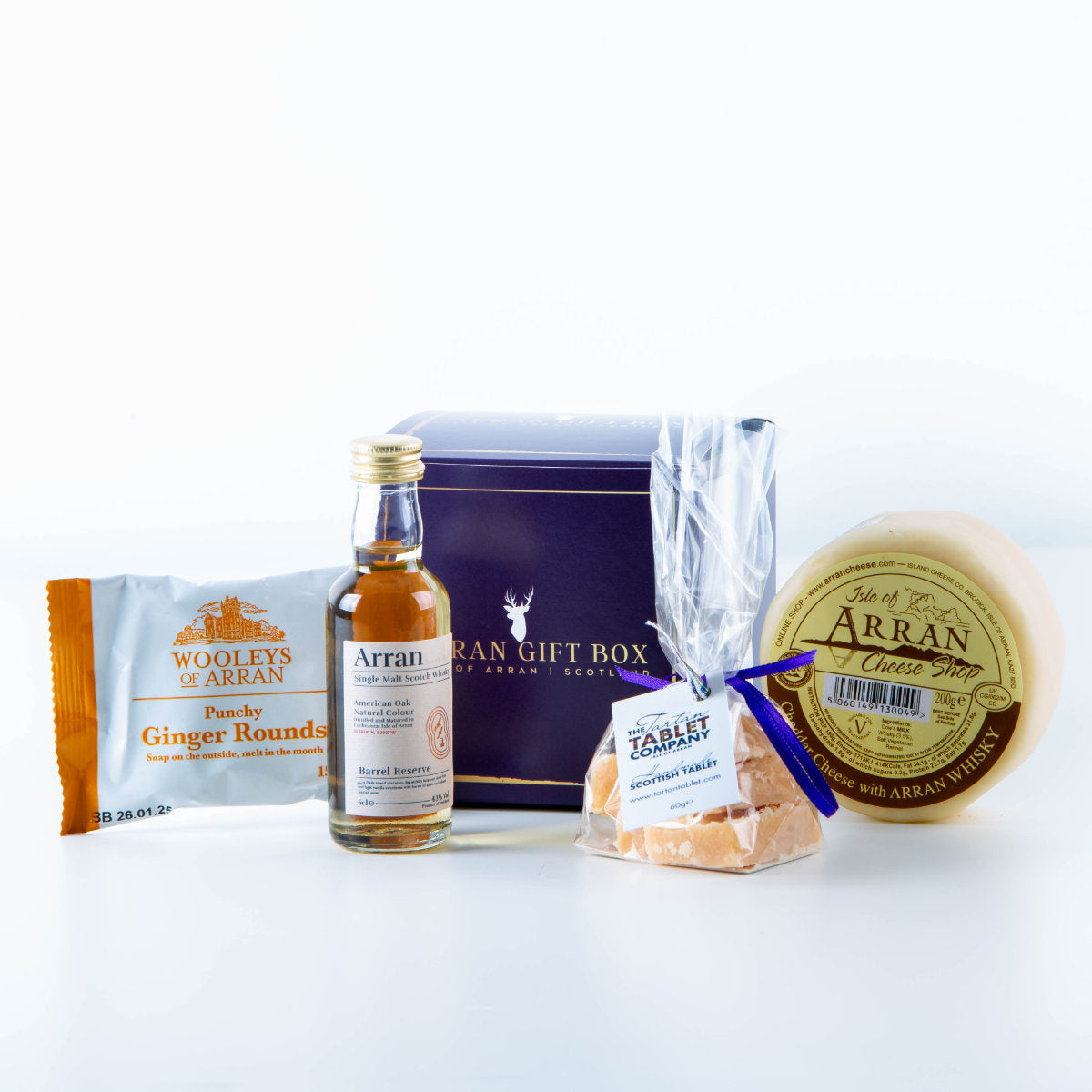 The Wee Whisky Lover (10 Year Old Malt) Arran Gift Box features Wooley's ginger rounds, a small bottle of Arran Whisky, a bag of vanilla fudge, and a wedge of Whisky Cheddar, all elegantly displayed on a light surface.