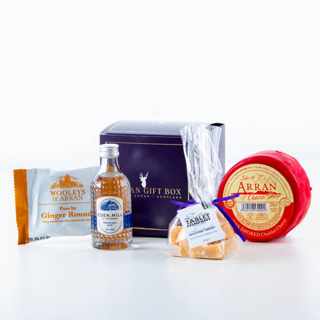 The Wee Gin Lover Arran Gift Box includes a small bottle of Eden Mill gin infused with botanical flavors, Woolley's ginger biscuits, a red wax-wrapped round of Isle of Arran cheese, and a clear bag of Arran Tablet fudge, all elegantly displayed against a white backdrop.