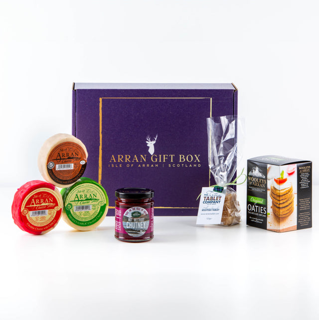 The "Original Big Taste Arran Gift Box," attractively packaged with a purple exterior, includes Smokey Garlic Cheddar and Chilli Cheddar, three cheese rounds, a chutney jar, a tablet bag, and an oatcake box. These gourmet treats are tastefully presented in front of the gift box on a clean white background.