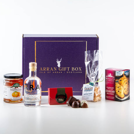 The Arran Gin Treat Box 20cl is perfect for gin enthusiasts, featuring orange marmalade, a small bottle of Arran gin, chocolates, traditional Scottish tablet, and cranberry rounds. These items are elegantly displayed in front of a purple box labeled "Arran Gift Box.