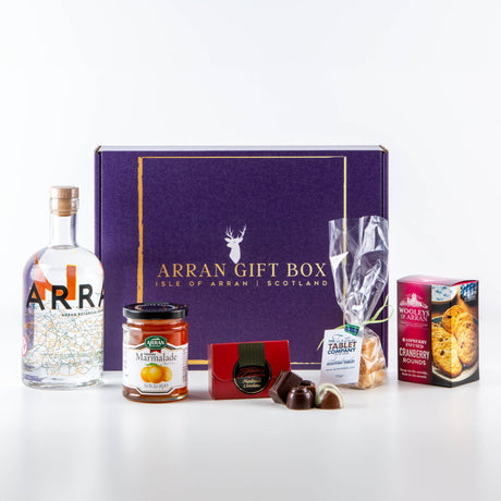 The "Deluxe Arran Gin Treat Box 70cl" is the perfect treat for any gin lover, featuring a bottle of Arran Gin, a jar of marmalade, assorted chocolates, a bag of tablet candy, and a box of cranberry rounds—all beautifully displayed to celebrate the flavors of the Isle of Arran.