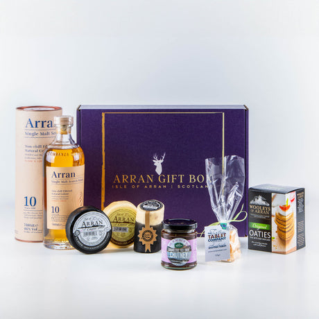 The Deluxe Whisky Lover (10 Year Old Malt) Arran Gift Box includes a bottle of Arran 10-year-old malt, oatcakes, chutney, cheese, and tablet pieces. It comes in an elegant dark purple box boldly displaying "Arran Gift Box," and features the distinctive Arran brand packaging.