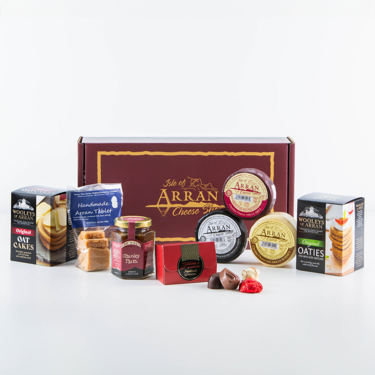 The Fireside Feast Box includes a selection of Arran cheddars, oatcakes, chutney, and chocolates. The display showcases various packaging and labels in front of a maroon box branded "Isle of Arran Cheese Shop.