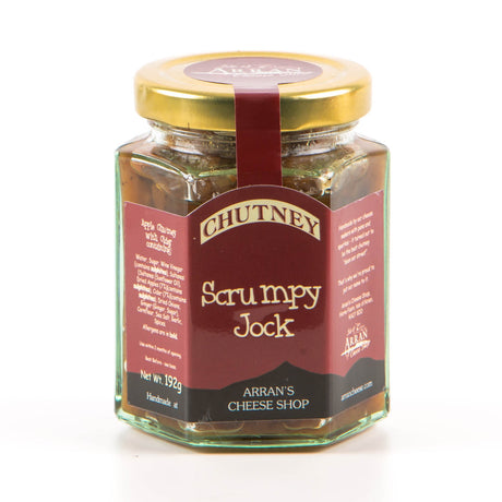 A jar of "Scrumpy Jock Apple & Cider Chutney" from Arran's Cheese Shop features local produce. The hexagonal glass jar with a gold lid has a red label that highlights ingredients such as apples, onions, and vinegar, all set against a white background.