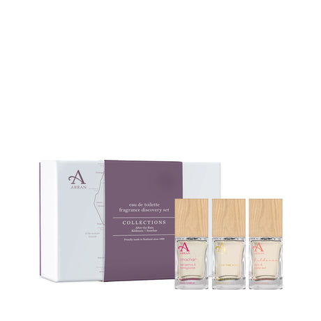 Displayed next to a purple and white box labeled "Arran Collections Fragrance Discovery Set" are three bottles from the Mixed Eau de Toilette Discovery Set, each topped with wooden caps. These bottles feature different fragrances, distinguishable by their unique labels.