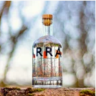 An Isle of Arran Gin 20cl clear glass bottle with a wooden cork is set on a mossy surface, capturing the essence of the isle’s wild botanicals. Bold, partially visible letters adorn it, while the softly blurred background features a bokeh effect with branches and light spots.