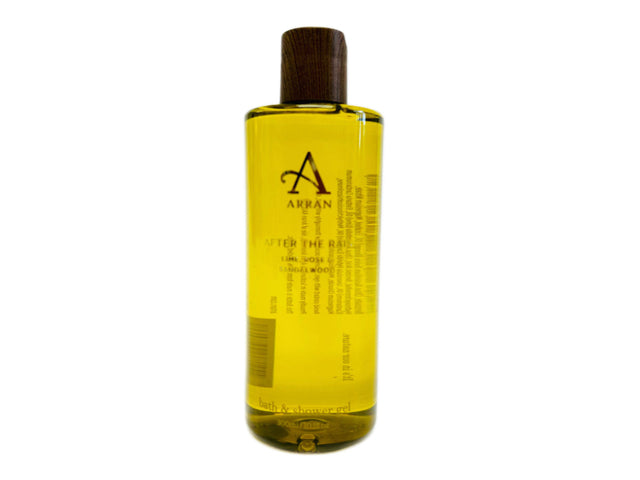 A 300ml clear bottle filled with yellow liquid, labeled "After the Rain Bath and Shower Gel." The label mentions sandalwood and is enriched with pro-vitamin B5. The bottle features a dark, wooden cap. Most of the detailed text on the label is in black and white, though some parts are unreadable due to the angle and lighting.