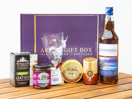 Discover the Deluxe Whisky Lover Gift Box, featuring Isle of Arran specialties: a bottle of Lochranza whisky, oatcakes, Arran chutney, cheese, honey, and tablet fudge. The elegant purple box is inscribed with "Arran Gift Box, Isle of Arran, Scotland," and beautifully presented on a wooden surface.