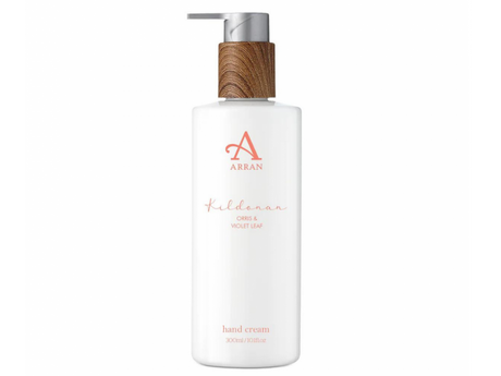 A 300ml bottle of Kildonan Hand Cream with a wooden pump top. The label displays "Kildonan - Orris & Violet Leaf" and emphasizes its rich moisturizing formula, with a minimalist design featuring a subtle pink logo and text on a white background.