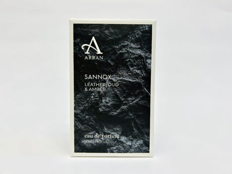 A perfume box featuring a textured black design highlights the brand "Arran" and the perfume "Sannox" in crisp white text. Boasting an invigorating scent of leather, oud, and amber, this Eau De Parfum is offered in 50ml packaging for those who appreciate sophistication.