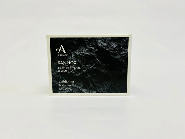 Arran's "Sannox Exfoliating Body Bar Soap 200g" for men comes in striking black packaging. Weighing 200g/7oz, it boasts an invigorating scent of leather, oud, and amber, perfectly showcased against a white background.