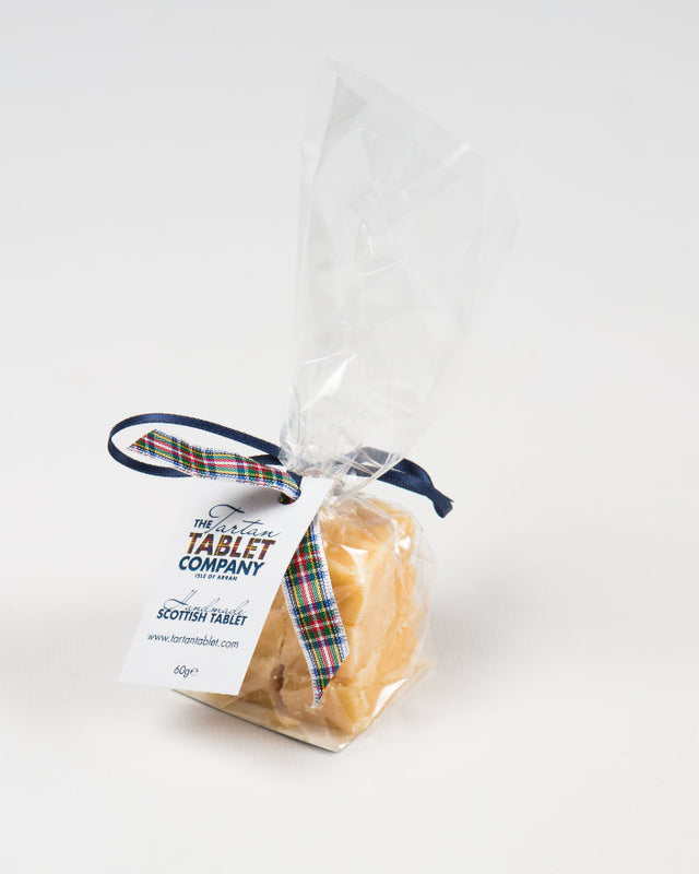 A clear bag of Arran Gold Scottish Tablet weighing 120g, tied with a tartan ribbon and featuring a branded label from The Ochil Tablet Company. The bag is set against a plain white background.