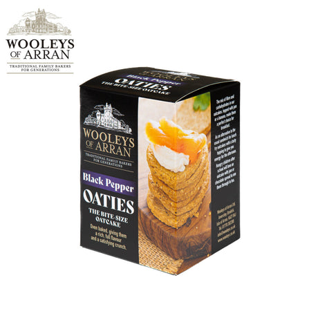 A box of Wooleys of Arran Black Pepper Oaties presents a perfectly arranged stack of oatcakes topped with cheese. The packaging emphasizes their bite-size, crunchy texture and traditional baking method, ensuring a delightful snack experience.