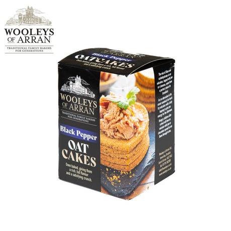 The image features a box of Wooleys of Arran Black Pepper Oatcakes, highlighting a stack of oatcakes adorned with a savory spread and garnish. The brand logo and information are clearly visible, offering the promise of a delightful peppery crunch in every bite.