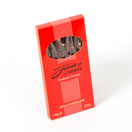 A James Chocolates Luxury bar of Chilli Chocolate is presented in a red rectangular box. The packaging features an oval window that provides a glimpse of the chocolates inside, elegantly labeled "Chilli Chocolate." This 100g box exudes luxury and delight.