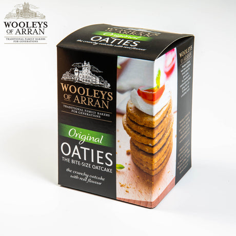 Wooleys of Arran Original Oaties are bite-sized oatcakes with a deliciously crunchy texture and rich flavour. The packaging displays stacked oatcakes adorned with cheese and a slice of tomato, making them ideal for any snacking occasion.