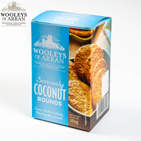 A box from the 12-pack of Wooleys of Arran Seriously Coconut Rounds features a blue and white design, adorned with an enticing image of the cookies. The packaging highlights "Snap on the outside, Melt in the mouth," with each box containing a net weight of 160g, embodying the essence of Arran Oatcakes in every bite.