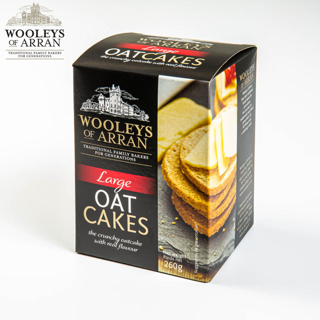 A box of Wooleys of Arran Original Oatcakes is showcased. The predominantly black packaging, which includes images of stacked oatcakes topped with cheese, emphasizes the iconic flavor and highlights its 260g weight with the tagline "The crunchy oatcake with real flavour.